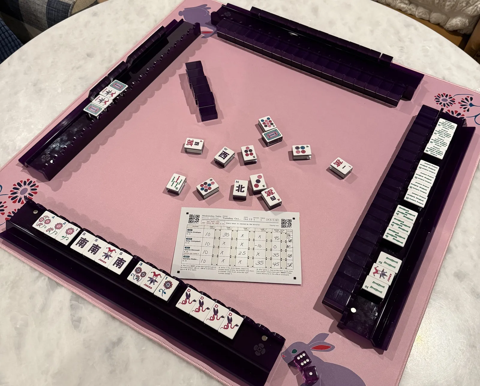 A mahjong table after a game, with an exposed hand on the front rack and a filled-in scorecard on the mat